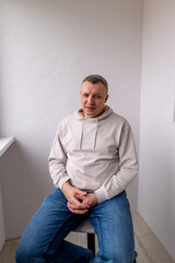 Portrait of a cheerful middle-aged man wearing a gray hoodie, standing against a textured stone...