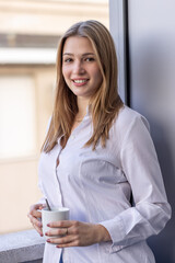 Young woman smiling while holding a cup of coffee on a balcony