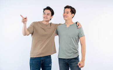 Fototapeta premium Two friends standing together, one pointing, smiling. Casual attire and warm companionship against a white background.