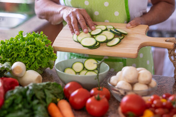 Close up on female hands holding a cutting board with sliced zucchini. Fresh raw vegetables on the table, vegan and healthy eating