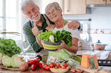 Attractive senior couple working together in home kitchen preparing vegetables. Caucasian elderly smiling people retirees enjoying healthy eating looking at camera