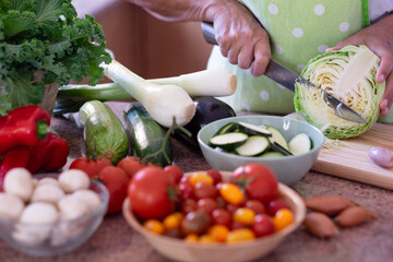 Close-up on senior woman's hand slicing a cabbage while preparing vegetables in home kitchen. Healthy, vegan or vegetarian eating