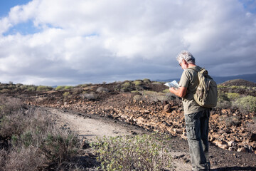Senior white haired man enjoying outdoor adventure stops checking a map. Active mature man in mountain and countryside excursion