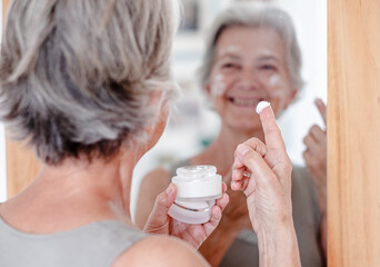 Close up shot of defocused senior beautiful woman applies anti aging cream on wrinkled face - elderly lady holding a cosmetic jar product