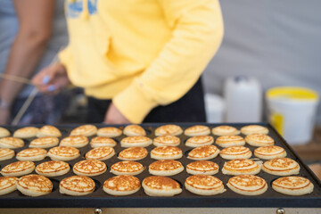 Typical Dutch poffertjes - tiny pancakes-being baked on a heavy cast iron pan being prepared during...