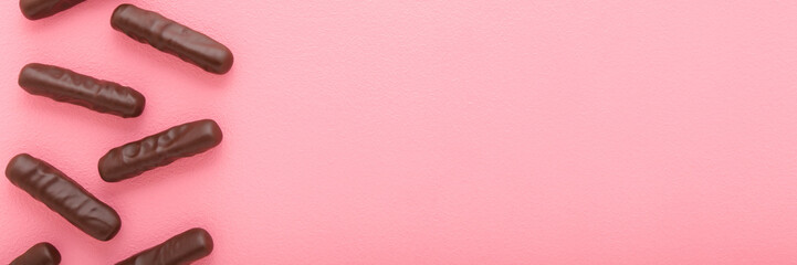 Long dark chocolate stick candies on light pink table background. Pastel color. Closeup. Sweet snack. Wide banner. Empty place for text. Top down view.