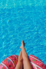 Pink inflatable ring floats close to female legs in turquoise swimming pool, playful summer energy radiating from vibrant accessory. Minimalist composition suits youth brands