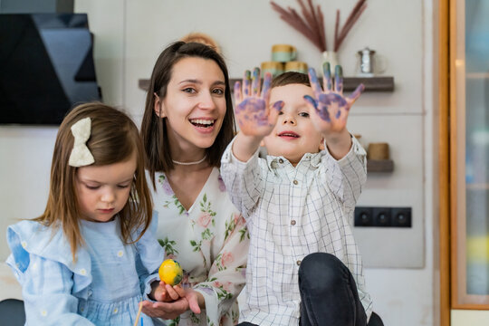 Family mother and children are having fun together in the kitchen coloring Easter eggs with paints and hands