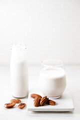 Pecan milk in a glass with raw pecan nuts on wooden table.