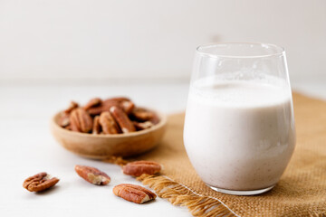 Pecan milk in a glass with raw pecan nuts on wooden table.