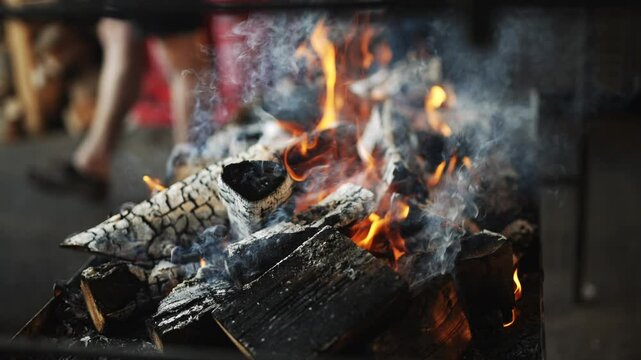A person is cooking food on a grill with a lot of smoke. The smoke is thick and the grill is full of wood