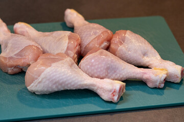 Close up of raw chicken drumstick on green plastic cutting board on kitchen table 