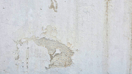 A close-up of a weathered concrete wall with peeling white paint, cracks, and exposed rough patches, showing signs of aging and deterioration