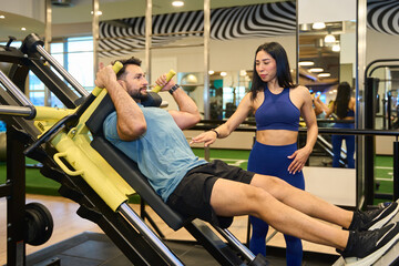 Personal trainer assisting client with leg press