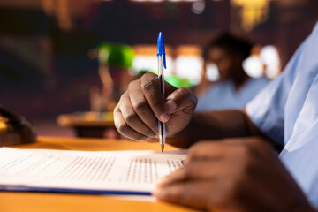 Black male pupil makes notations about practice methods to prepare for an exam, studying at the...