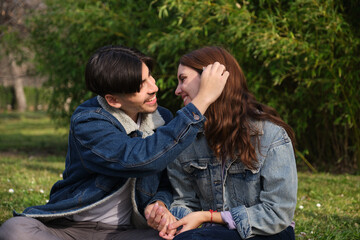 Fototapeta premium Romantic couple sitting on grass, holding hands and showing love and affection