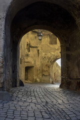 Obraz premium Arched passage with lantern over an old cobblestone street in ancient European city.