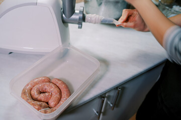 Cook corrects the intestine on the nozzle of the electric meat grinder next to the sausages in the...