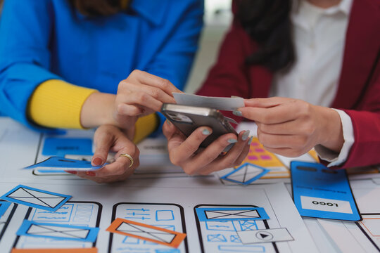 Ux designers working on mobile app interface using paper prototypes and smartphone