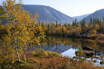Vibrant autumn foliage surrounding rocky khibiny mountains, reflecting pristine lake waters across kola peninsula's dramatic nordic landscape in northern russia