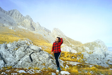 Naklejka premium Travel to the east of Montenegro: a full-length photograph of a female tourist under the peak of Kucki Kom during a hike in the Komovi Nature Park. Active recreation in autumn: a trip to the mountains