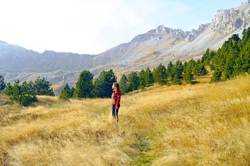 Fototapeta premium Woman enjoying the view in a beautiful location: a female hiker stands alone among the yellow grass against the backdrop of a coniferous forest and impressive mountain slopes in Komovi, Montenegro.