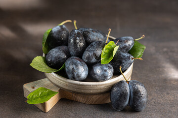Ripe plums glistening with moisture, nestled alongside verdant leaves in wooden bowl, capturing fresh harvest moment with rustic charm