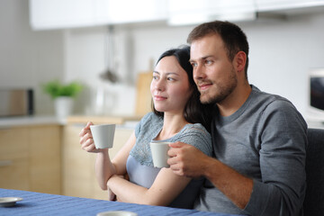 Interracial couple drinking looking away in a house interior