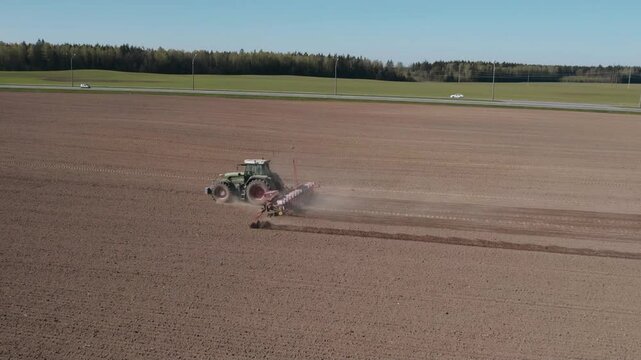 Tractor sowing potatoes in an agricultural field during springtime from above