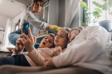 Children watching smartphone while mother cleaning home
