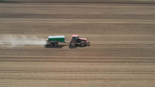 Tractor sowing potatoes in an agricultural field during springtime from above