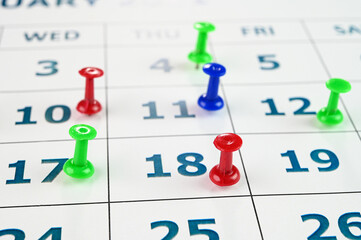 Multicolored thumbtacks on a monthly calendar.