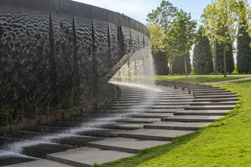 “Infinity” fountain in form of huge bowl is located in public park “Krasnodar” or “Galician Park”. Waterfall flows in streams into granite bed of artificial river. Krasnodar, Russia - May 5, 2024
