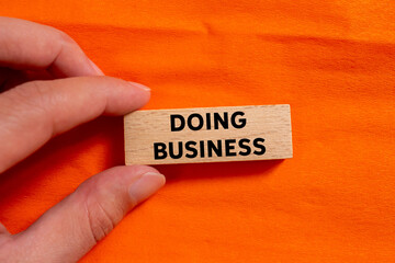 Doing business message written on wooden block on orange background. Conceptual doing business...