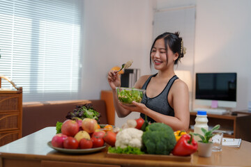 Young asian woman eating fresh vegetable salad in living room