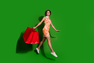 Full body photo of pretty young girl shopping bags running wear trendy colorful outfit isolated on green color background