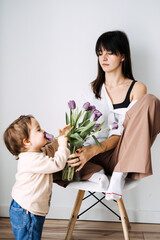 Mother and daughter with vase of tulips, sharing a calm moment. Modern motherhood, floral...