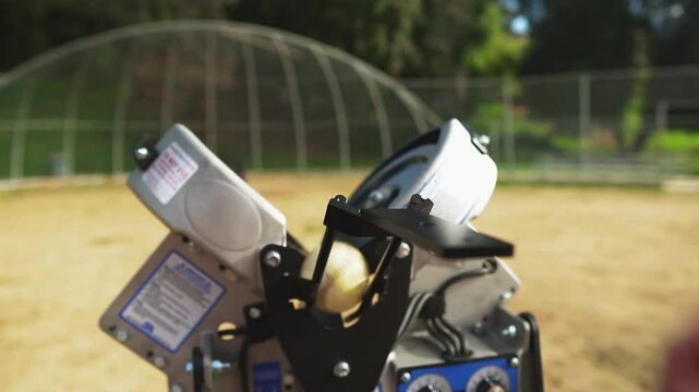 Hand drops baseball into fast pitching machine, showcasing high speed precision, medium static
