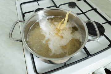 A stainless steel pot filled with boiling water and pasta sits on a lit gas stove. 