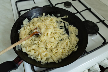 The cooked pasta is in a black frying pan on the gas stove.