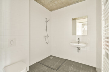 A clean and modern bathroom with white tiles, a sleek shower, a sink with a mirror, and minimalist design elements emphasizing simplicity.