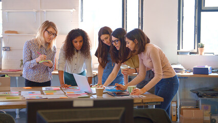 Multi-Cultural Female Business Team Meeting In Office Looking At Laptop And Documents