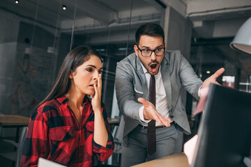 Angry young european man boss scolds to frightened shocked sad manager lady at workplace with computer due to mistake in office interior. Problems in business, work in company, stress and pressure