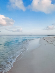Imagine a stunningly beautiful beach where gentle waves gracefully roll onto the golden sand, beneath a wide open blue sky decorated with fluffy white clouds scattered throughout