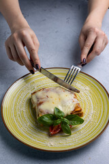 Italian lasagna on a blue plate with a fork and basil leaf