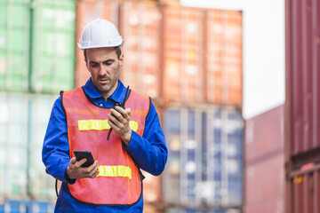 Foreman in hardhat and in safety gear talks on two-way radio control loading containers box from...