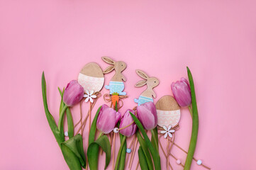 Purple tulips, egg, wooden Easter bunnies on the pink background. Flat lay, top view.