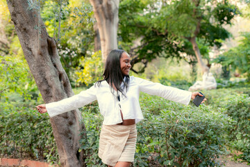Carefree young woman enjoying freedom in green park holding smartphone
