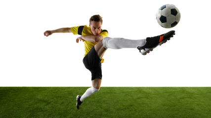 Side view of focused young man, soccer player performing acrobatic high kick, lifting leg towards ball, focusing intensely against white background. Concept of dynamic movement, competition, training.