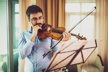 Man playing violin at home. He is practicing for live performance.